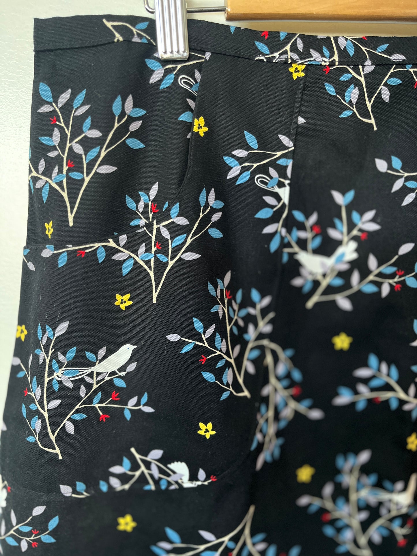 Black shorts with colorful floral and bird pattern on a hanger.