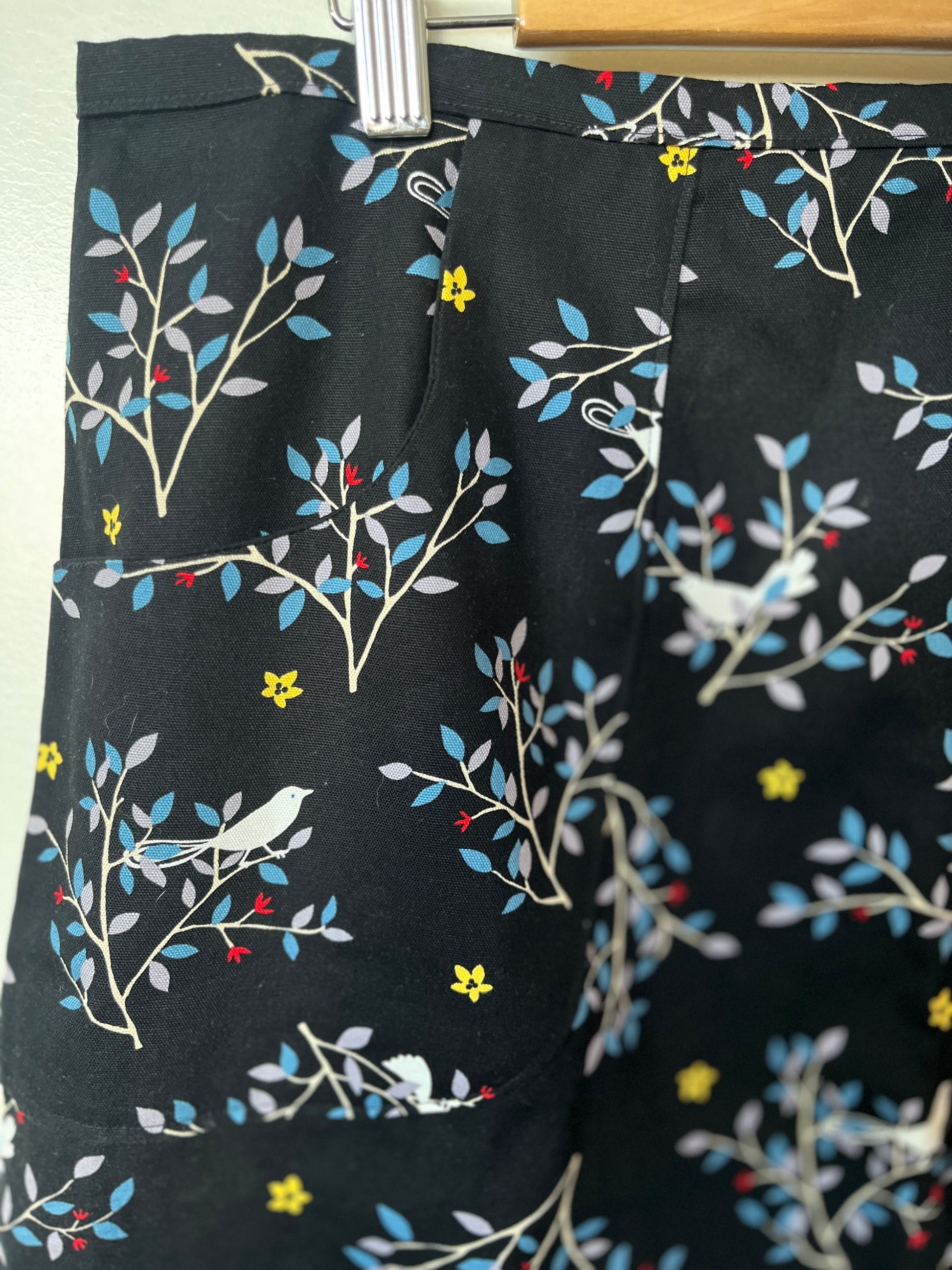 Black shorts with colorful floral and bird pattern on a hanger.