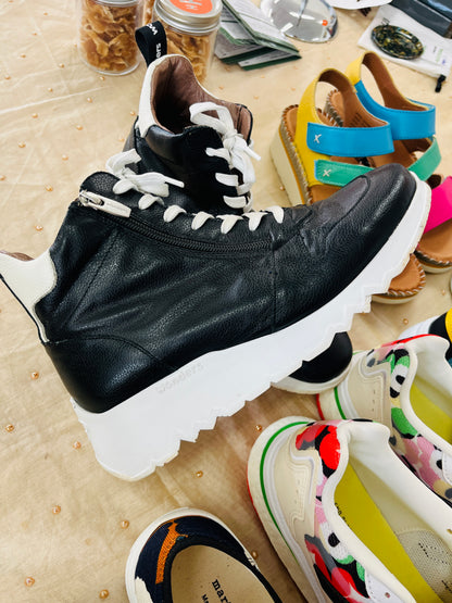 Black leather boot with white sole on a wooden surface