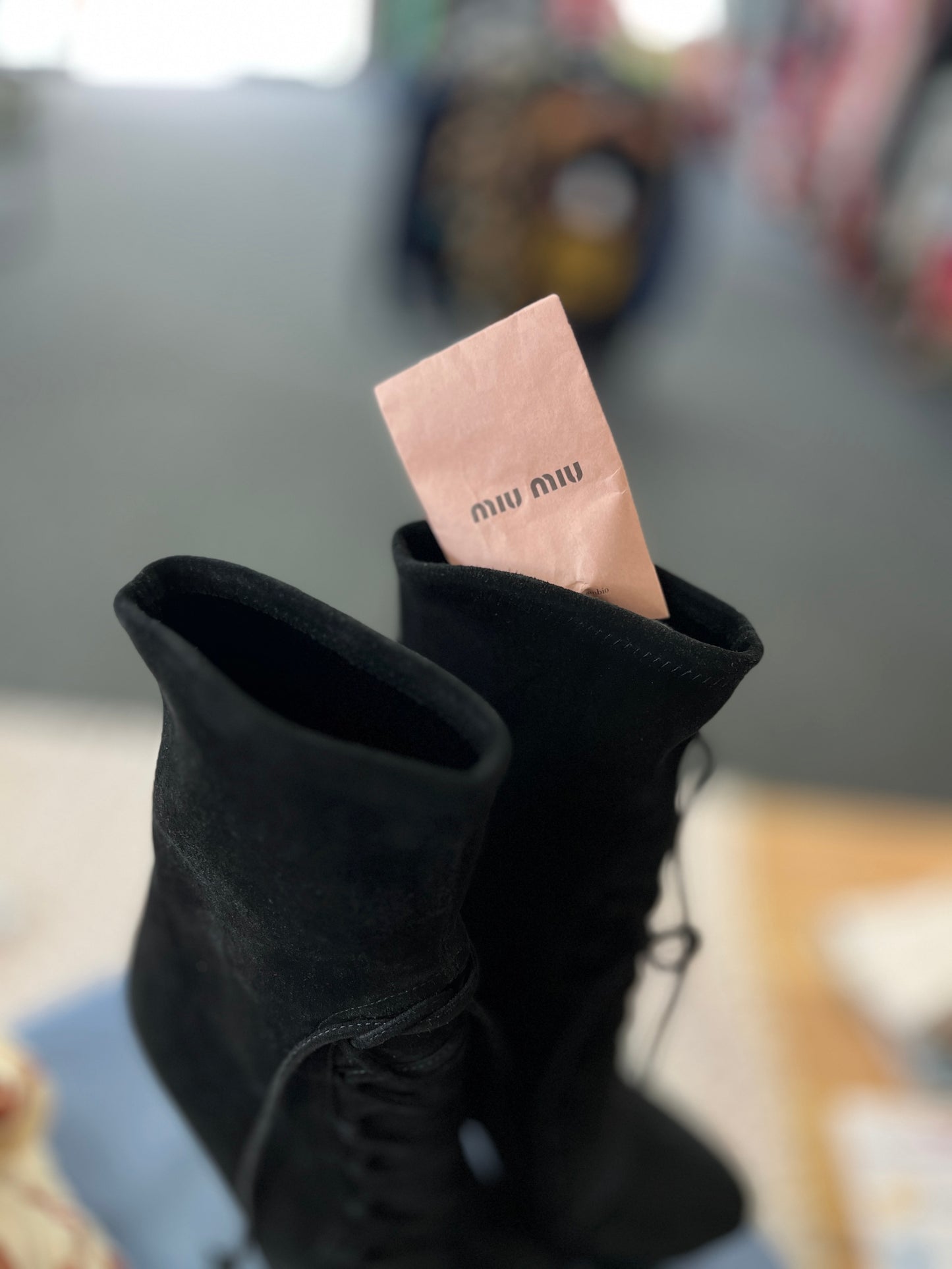Black high-heeled boots with a pink 'Miu Miu' card inside, blurred background